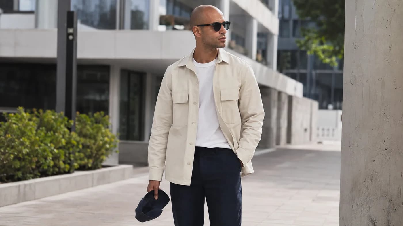 Bald man holding a cap in a polished hat-free outdoor outfit